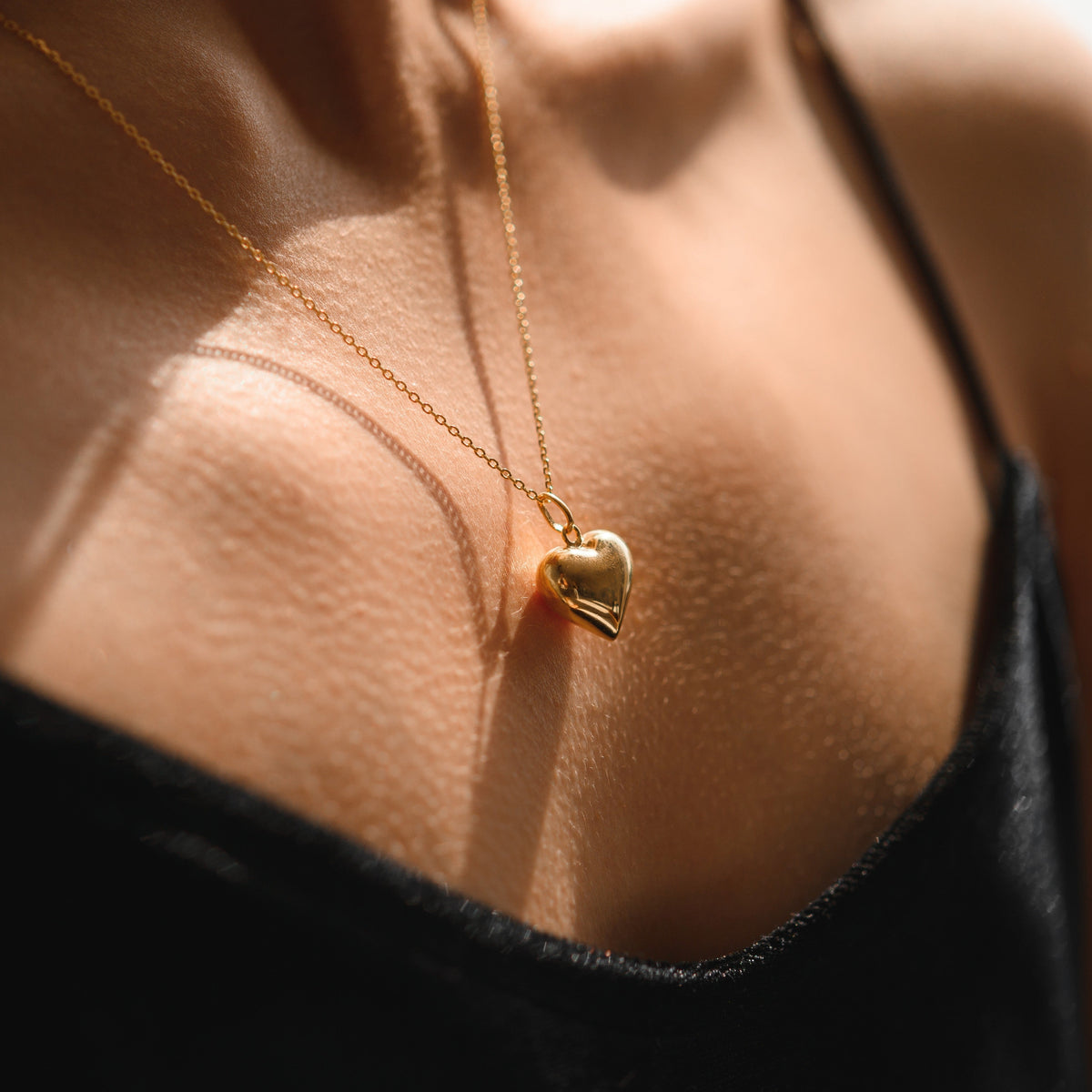 A close-up image of a person wearing a gold-plated heart-shaped necklace on a chain, positioned against skin tones.